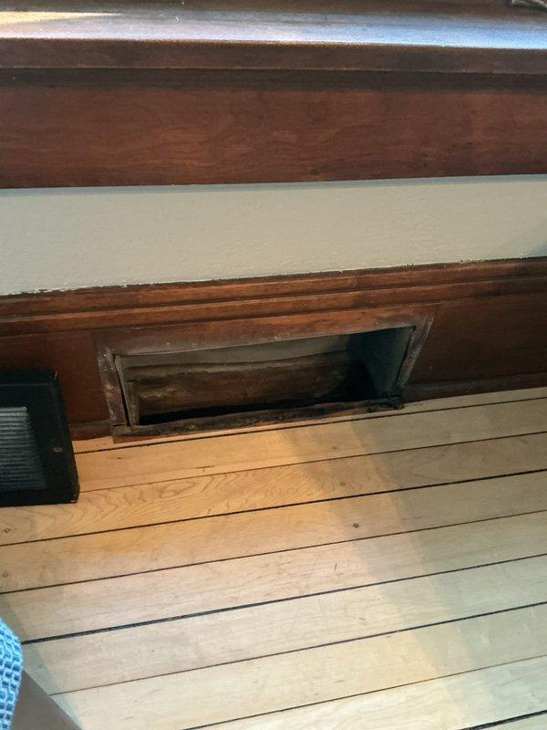 Inspected recessed HVAC vent installation in wooden wall panel. Observed proper alignment of register opening with minimal dust accumulation. Verified correct air flow through the return air vent and confirmed architectural integration with existing woodwork was intact.