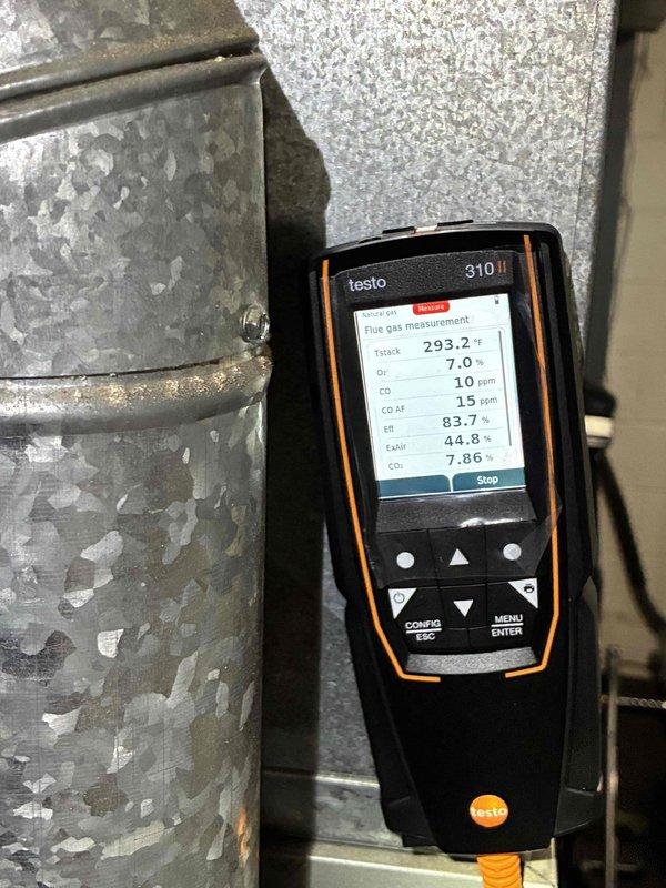 Performed combustion analysis on heating system using Testo 310 gas analyzer, documenting flue gas readings including stack temperature (293.2°F), oxygen (7.0%), CO (10 ppm), and efficiency (44.8%). Inspected burner assembly and verified proper flame characteristics with three blue flames visible through heat exchanger tubes, indicating normal operation after addressing the no heat complaint.