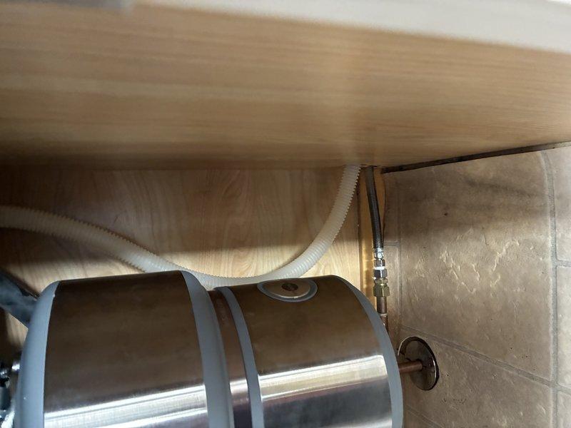 Completed inspection of under-sink plumbing installation. Assessed garbage disposal unit and drainage configuration, including corrugated drain hose routing. Examined connection points to wall plumbing, confirming proper installation of brass/copper fittings and ensuring secure attachment of all components.