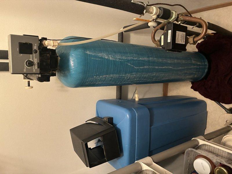 Successfully installed a complete water treatment system in the utility area, consisting of a primary blue cylindrical water filter tank with digital control valve and a blue rectangular water softener with brine tank. System was properly connected to the existing copper supply lines with appropriate PVC fittings, ensuring proper functionality and optimal water quality for the residence.