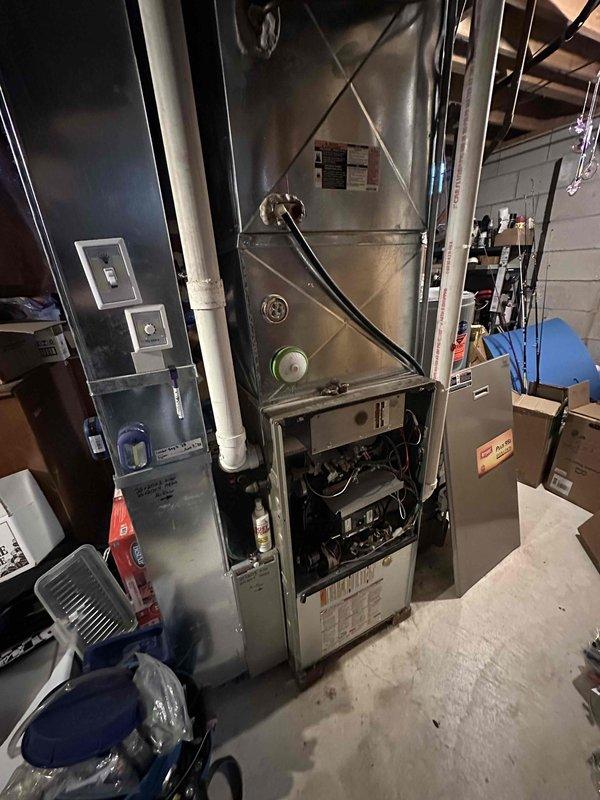 Conducted comprehensive evaluation of aging HVAC system in basement mechanical room, including assessment of furnace unit with visible control panels and wiring, along with adjacent water heater installation with associated copper and PVC piping. Documentation completed with detailed photographs of current equipment to support replacement recommendation, noting configuration of existing ductwork, ventilation systems, and utility connections necessary for proper system upgrade planning.