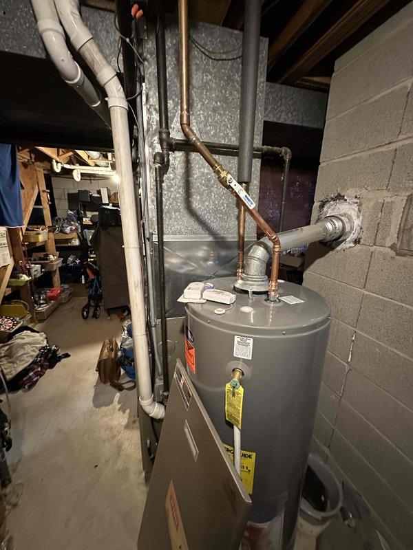 Conducted comprehensive evaluation of aging HVAC system in basement mechanical room, including assessment of furnace unit with visible control panels and wiring, along with adjacent water heater installation with associated copper and PVC piping. Documentation completed with detailed photographs of current equipment to support replacement recommendation, noting configuration of existing ductwork, ventilation systems, and utility connections necessary for proper system upgrade planning.