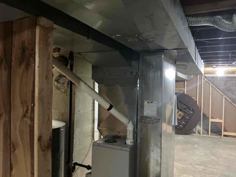 Conducted inspection and provided estimate for replacement of outdated HVAC system in unfinished basement area. Current installation shows galvanized ductwork with white PVC venting pipes connected to existing air handler. Proposed replacement includes new furnace unit to be installed between wooden framing studs with proper connections to existing ductwork and venting system.