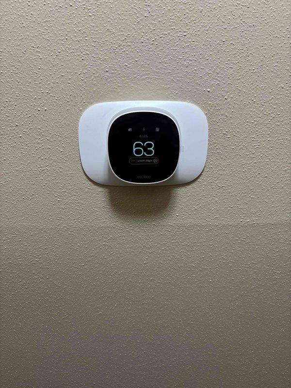 Successfully installed complete HVAC system including outdoor heat pump/AC unit mounted on concrete pad with proper refrigerant line connections. System includes modern digital programmable thermostat set to 63°F, with all components tested and functioning correctly.