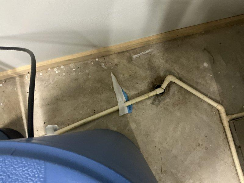 Completed assessment of water heater system in basement utility area. Observed PVC drainage pipe with visible mineral deposits on concrete floor and inspected vertical metal duct system with black foam insulation sleeves. Noted copper pipe branching horizontally from main assembly requiring attention.