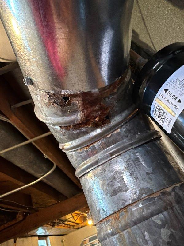 Inspected furnace system and discovered severe corrosion damage in the ductwork, particularly at connection points and a 90-degree elbow joint where complete metal failure has occurred. Documented extensive rust deterioration with multiple perforations that are compromising system integrity and efficiency. Recommended immediate replacement of affected ductwork sections to prevent further deterioration and potential safety hazards.