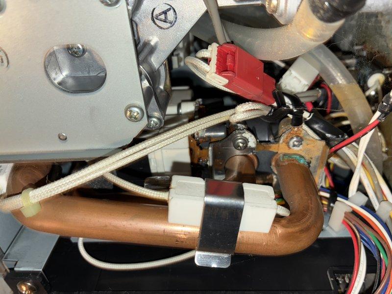 Performed diagnostic inspection on tankless water heater, examining internal components including heat exchanger, circuit board, and copper piping connections. Removed cover to access and evaluate electronic components, focusing on the control board with multiple colored wiring connections. Inspected L-shaped copper pipe assembly and associated clamps for proper installation and potential leaks. System was reassembled after verification of proper operation.