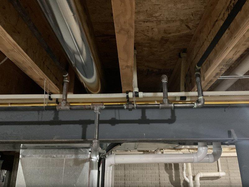 Conducted assessment of existing gas line infrastructure in unfinished basement area. Inspected horizontal pipe runs along ceiling joists and examined connection points to furnace unit. Evaluated potential installation pathway for new gas line, noting structural considerations around I-beam and existing utility configurations. Photos documented current plumbing layout and HVAC equipment positioning for proper gas line sizing and placement.