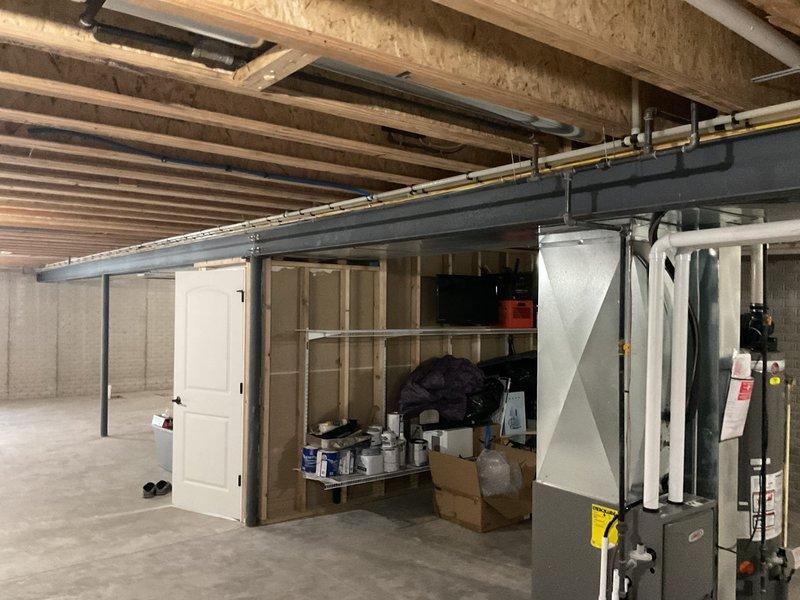 Conducted assessment of existing gas line infrastructure in unfinished basement area. Inspected horizontal pipe runs along ceiling joists and examined connection points to furnace unit. Evaluated potential installation pathway for new gas line, noting structural considerations around I-beam and existing utility configurations. Photos documented current plumbing layout and HVAC equipment positioning for proper gas line sizing and placement.