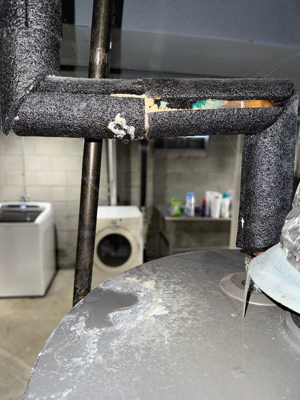 Conducted inspection of Rheem Performance water heater showing significant corrosion, mineral buildup, and white calcium deposits around top connection points. Noted damaged black foam pipe insulation with visible splits exposing underlying material. Observed possible leakage or condensation issues evidenced by white streaking down tank sides, indicating system requires replacement due to age-related deterioration.