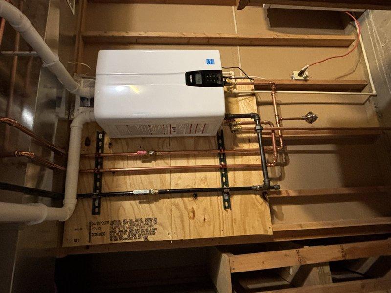 Completed installation of a new tankless water heater unit in utility area. Mounted unit on plywood backing board against wooden framed wall using proper metal brackets. Connected copper supply lines with appropriate shut-off valves and installed necessary electrical connections to exterior meter box. All systems tested and functioning properly.