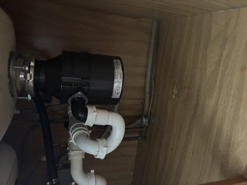 Inspected and documented customer's stainless steel sink with existing garbage disposal installation. System includes black disposal unit with proper rubber flaps in drain opening, connected to white PVC drain assembly with standard P-trap configuration. All components appear functional with normal wear patterns visible on sink surface.