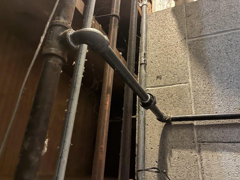 Installed black iron gas piping system with appropriate elbows and fittings, including both horizontal and vertical runs secured against concrete block wall. Completed all connections with proper threading and ensured system integrity through thorough leak testing of all joints and connection points.