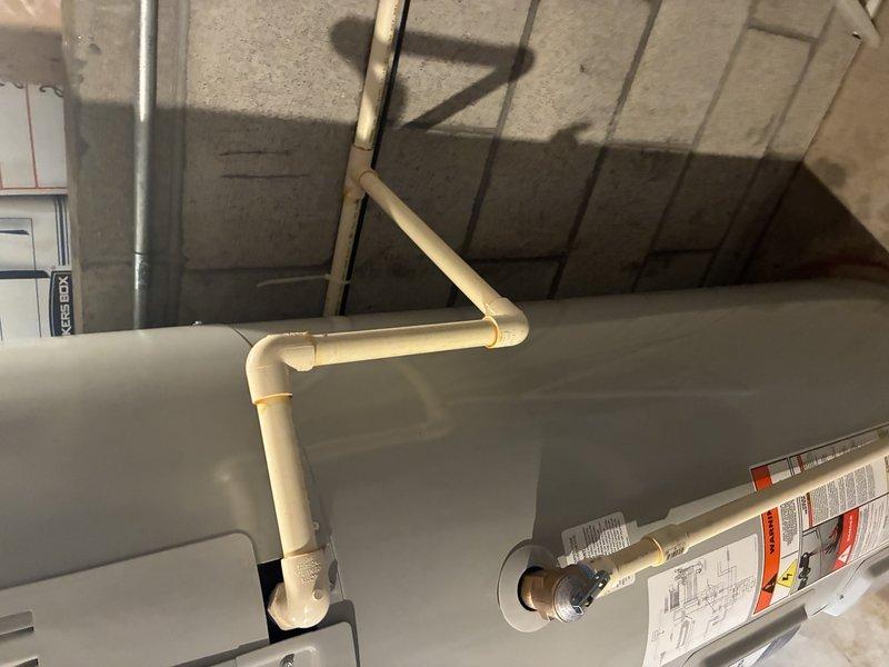 Completed installation of a tanked water heater system with associated PVC drainage piping and copper supply lines. Installed pressure regulator with float valve on the cold water inlet and properly connected all necessary brass fittings and valves for optimal system operation.