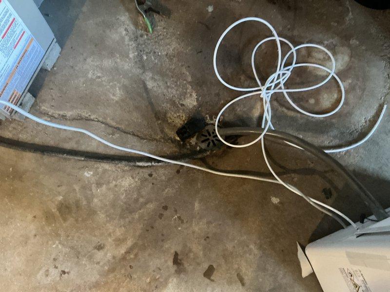 Conducted assessment of basement HVAC installation area featuring concrete flooring with existing drain access. Documented current air handler configuration with foil-faced insulated ductwork connected to vertical furnace unit. Evaluation completed for replacement estimate of aging system in utility room with concrete block walls.