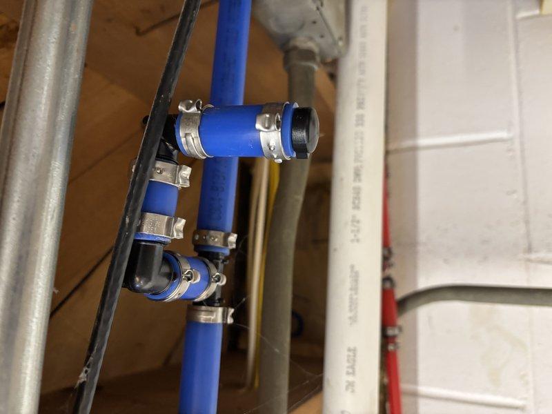 Inspected residential plumbing system and evaluated water heater installation requirements. Observed existing PEX piping configuration with proper metal clamp supports and examined ventilation ducting with appropriate clearance. Noted yellow insulation material in surrounding cavity spaces. System appears well-organized with standard connections and fittings for residential water heater installation.