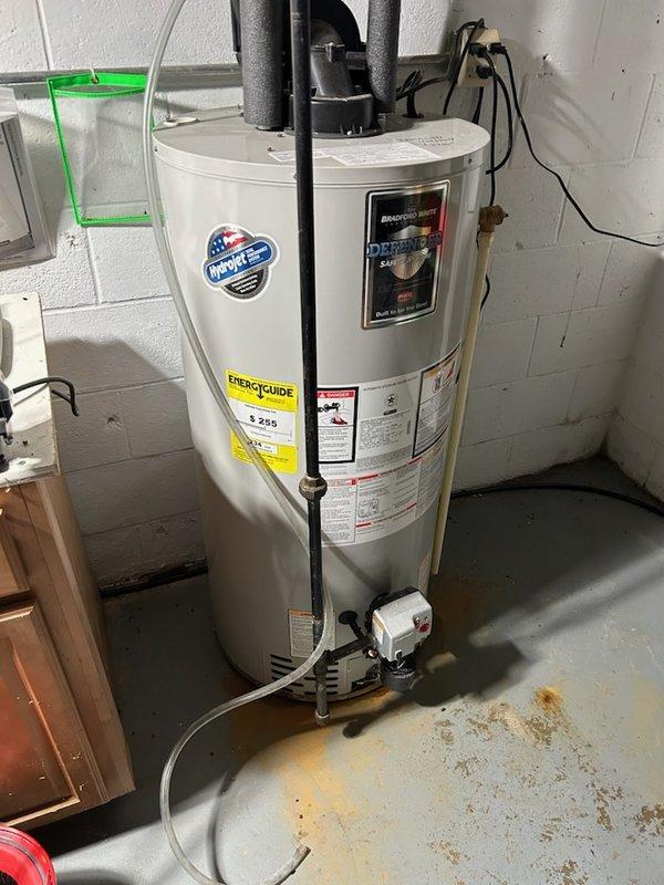 Performed visual inspection of Bradford White residential water heater in utility area. Observed normal installation with proper pipe connections and venting. Noted minor floor staining beneath unit, potentially indicating previous leakage that should be monitored.