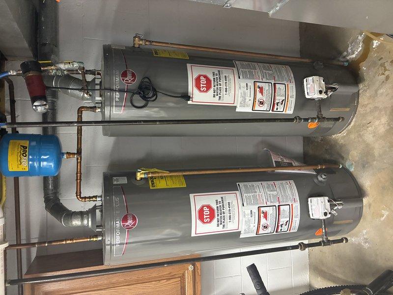 Performed installation of two tanked water heaters with proper copper piping connections. System includes a blue expansion tank, temperature and pressure relief valves, and necessary control valves including a prominent yellow handle valve. Observed minor corrosion on some copper fittings. All components were verified to be functioning correctly with no leaks detected.