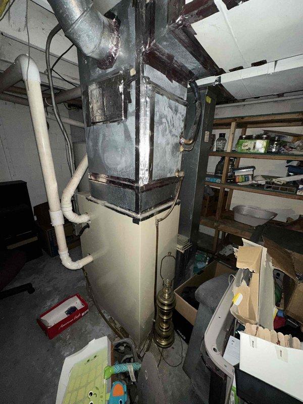 Conducted comprehensive assessment of aging HVAC system in basement utility area showing significant wear. Recommended full system replacement due to deteriorated ductwork with visible seams and compromised metal strapping. Exterior inspection revealed inadequate PVC ventilation configuration that doesn't meet current code requirements.