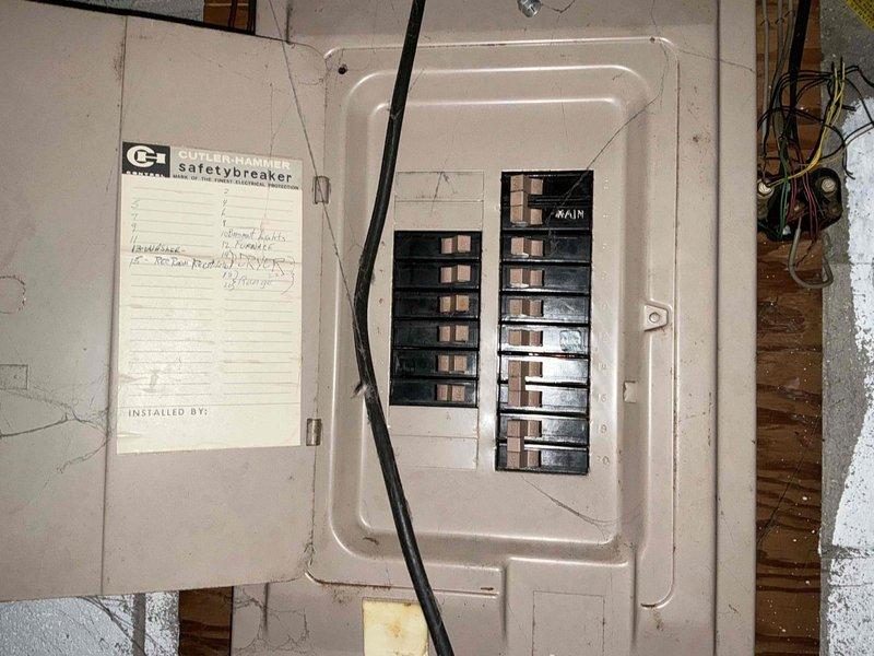 Performed inspection of GE electrical panel showing signs of age and wear. Panel has main breaker with handwritten circuit directory and visible wiring extending from top. Adjacent Lennox HVAC system was noted with insulated ductwork and associated piping. No electrical modifications were made at this time; assessment completed for future fixture and outlet installation planning.