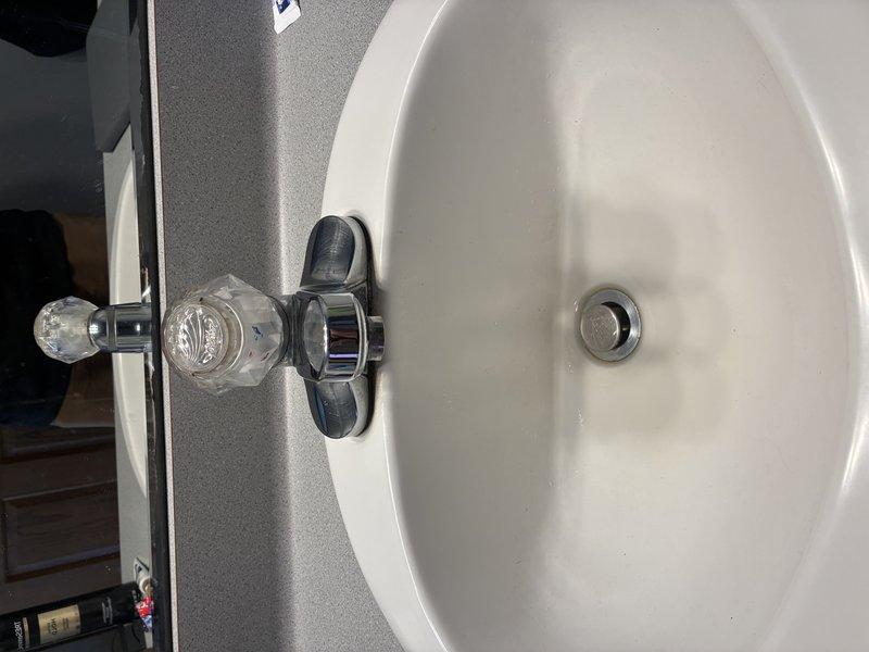Completed inspection of bathroom sink fixture with crystal/acrylic handle faucet mounted on white porcelain bowl sink. Verified proper function of chrome drain and transparent cold water control knob. No issues detected with the fixture or surrounding countertop installation.