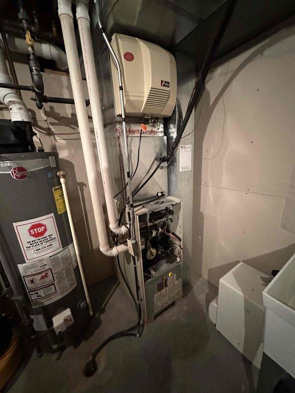 Conducted inspection of existing HVAC system for potential replacement. Examined electrical panel to verify adequate capacity for new equipment. Accessed furnace unit with front panel removed to evaluate internal components and wiring condition. Documented current setup including water heater proximity and PVC ventilation/drainage configuration to determine optimal replacement strategy.