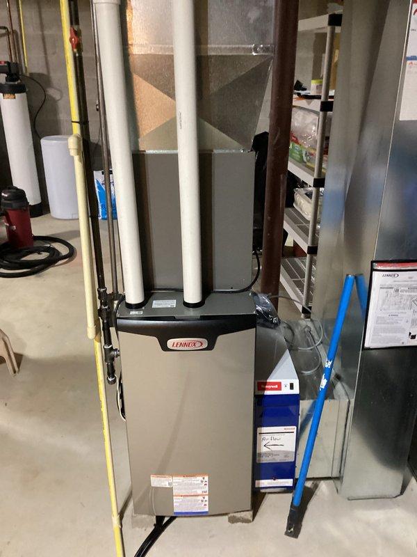 Completed installation of a new Lennox furnace system in basement utility area. System includes proper connection to existing ductwork with vertical exhaust pipes and air return plenum. Installation included setting up the air handler component with appropriate filtration system and verifying all connections meet professional standards.