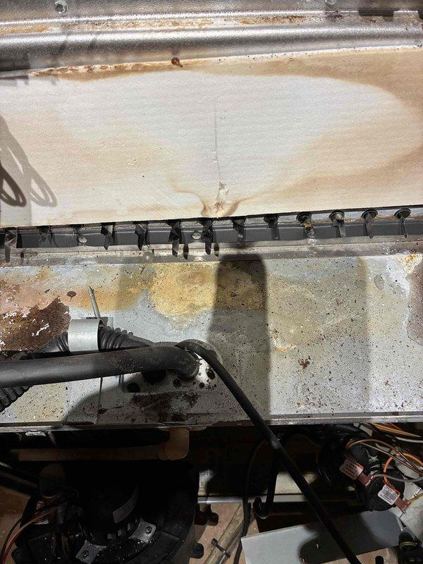 Performed routine tune-up on HVAC system, discovering significant corrosion on mounting bracket and interior components. Removed and replaced deteriorated bracket assembly showing rust damage at connection points, and cleaned accumulated rust stains and water damage from interior housing panel. System now operating within normal parameters after component replacement.