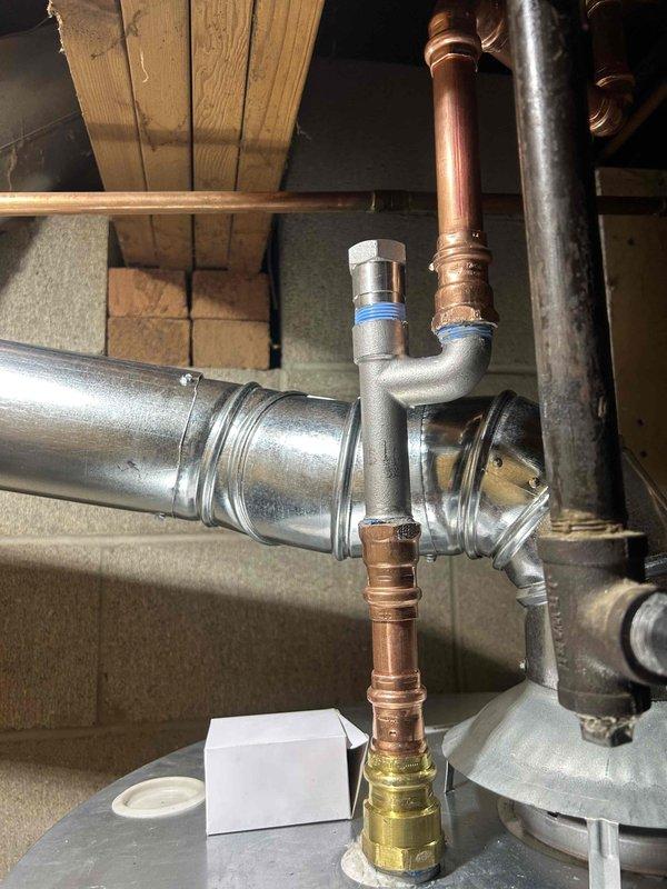 Installed new plumbing assembly in utility area including galvanized steel Y-junction with blue ring connector and copper piping. Integrated system includes brass fittings and a red-handled shutoff valve for improved flow control. All connections properly soldered with no leaks observed upon final inspection.