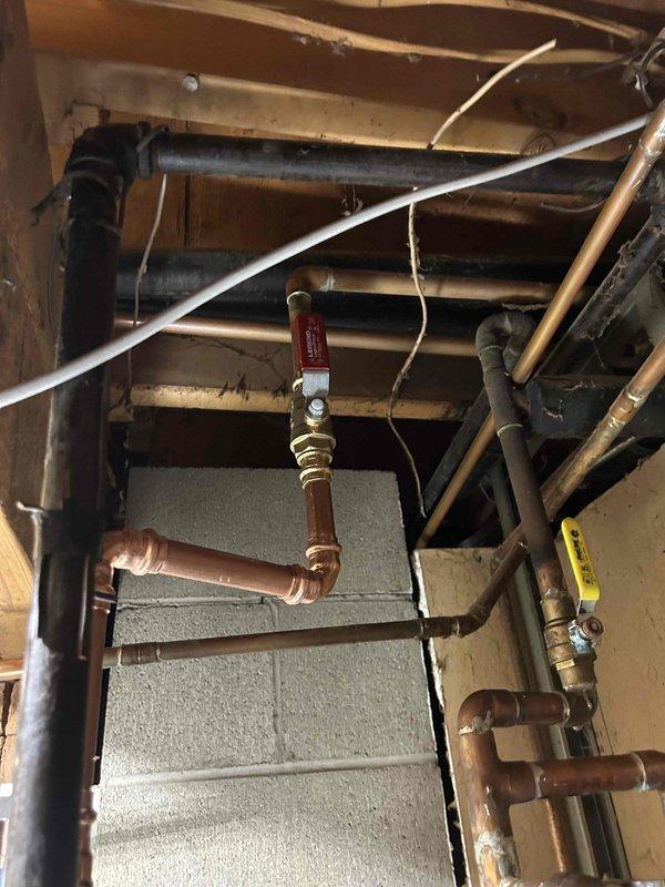 Installed new plumbing assembly in utility area including galvanized steel Y-junction with blue ring connector and copper piping. Integrated system includes brass fittings and a red-handled shutoff valve for improved flow control. All connections properly soldered with no leaks observed upon final inspection.
