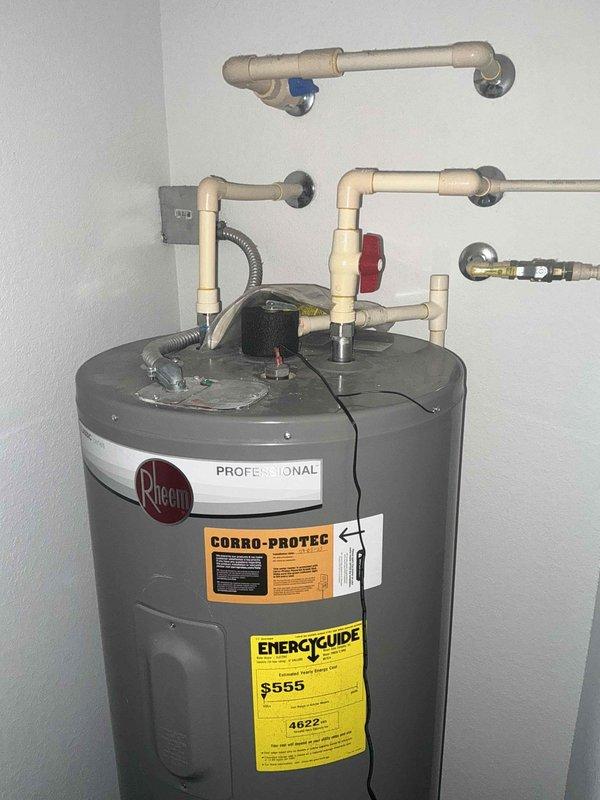 Completed installation of a Rheem Professional water heater in utility area. System includes PVC piping configuration with appropriate valves and wall penetrations. Installed all necessary connections including supply lines, drainage components, and verified proper electrical hookup via flexible conduit.