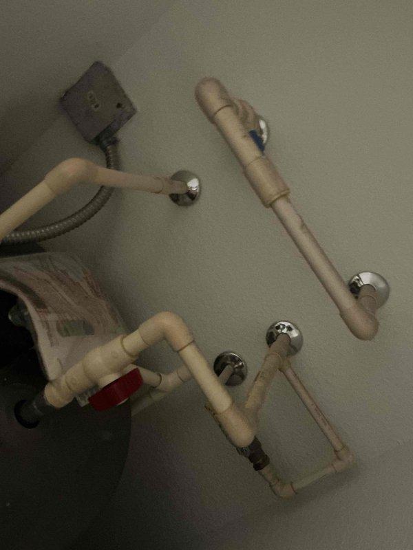 Completed installation of a Rheem Professional water heater in utility area. System includes PVC piping configuration with appropriate valves and wall penetrations. Installed all necessary connections including supply lines, drainage components, and verified proper electrical hookup via flexible conduit.