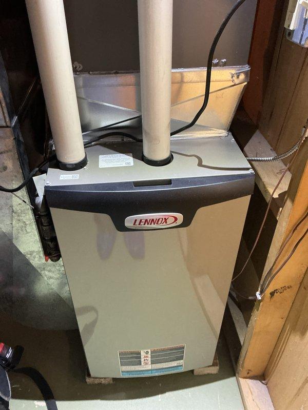 Performed routine tune-up service on a Lennox furnace system located in basement utility area. Inspected and verified proper operation of all components including the venting system with PVC exhaust/intake pipes. Checked connections to ductwork and examined Thiele system labels for specifications during maintenance procedure.