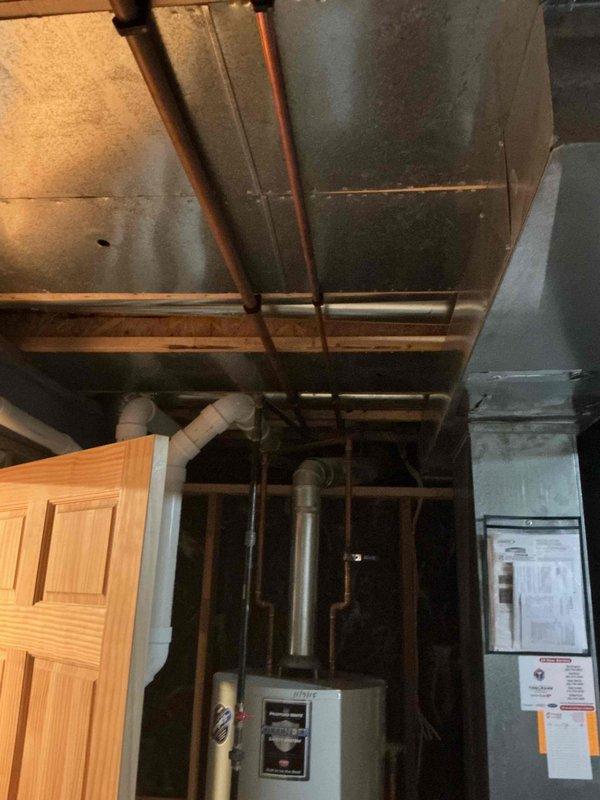 Performed assessment of existing water heater installation in residential basement. Inspected PVC drainage system with P-trap configuration and associated drain lines. Evaluated copper supply piping and metal vent pipe for proper installation and code compliance. Noted unit installation appears to date from 2003 based on visible date stamp on structural framing.