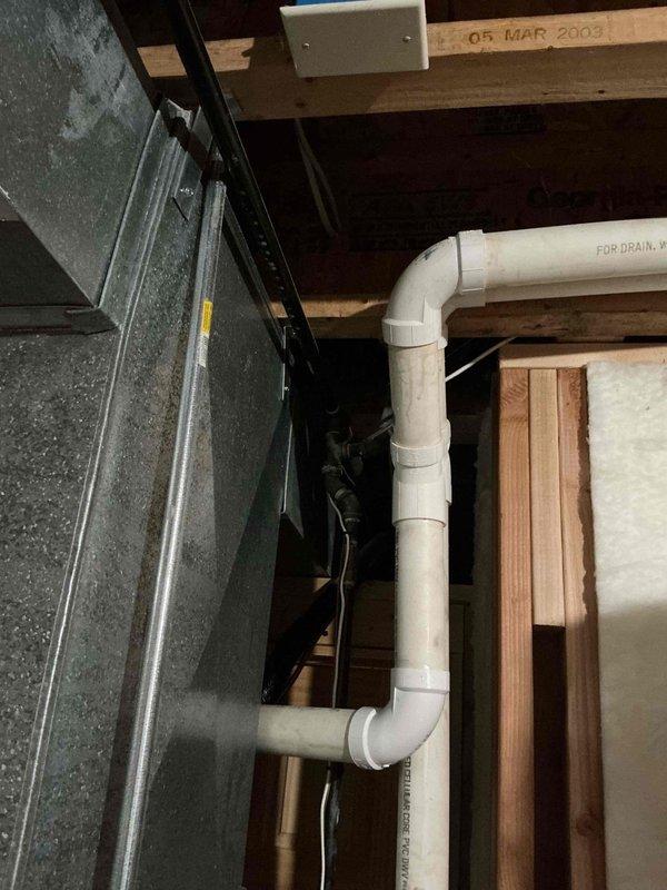 Performed assessment of existing water heater installation in residential basement. Inspected PVC drainage system with P-trap configuration and associated drain lines. Evaluated copper supply piping and metal vent pipe for proper installation and code compliance. Noted unit installation appears to date from 2003 based on visible date stamp on structural framing.