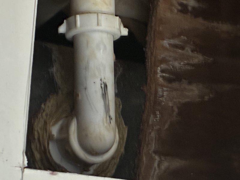 Repaired leaking P-trap assembly in bathroom sink drain system. Removed corroded PVC pipe section showing visible water damage and staining around connection points. Installed new P-trap with proper threaded coupling to eliminate leak and prevent sewer gas intrusion.