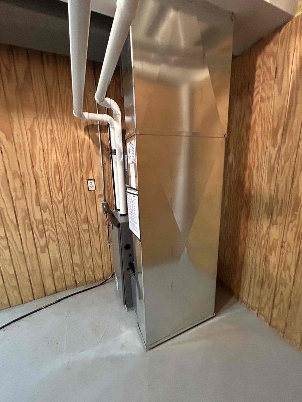 Completed installation of a new Lennox HVAC complete system in the utility area. Mounted main furnace unit on concrete floor against wood-paneled wall, connected proper PVC ventilation piping with multiple elbows extending upward. Installed and connected all required ductwork with appropriate metal fittings to ensure optimal system performance.