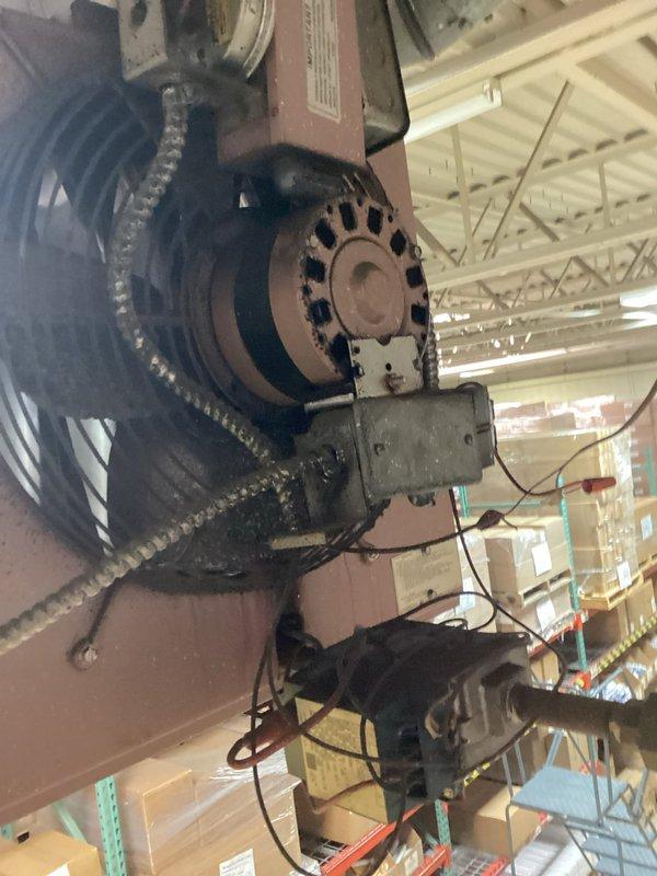 Inspected industrial HVAC unit (labeled "M5") in warehouse environment. Examined motor assembly and belt drive system components for proper operation. Noted dust accumulation on equipment and verified integrity of electrical connections to the blower motor and drive mechanism.