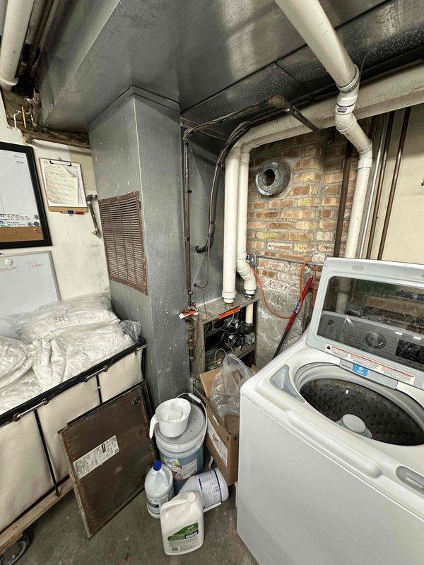 Conducted inspection of commercial laundry facility's HVAC system. Evaluated existing furnace unit showing signs of age and inefficiency, positioned adjacent to washing machines in utility room. Recommended replacement of current system with appropriate commercial-grade unit to ensure proper ventilation and improve energy efficiency in the confined brick-walled mechanical space.