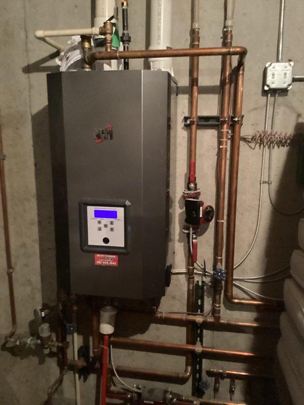 Performed inspection of basement furnace installation, noting proper mounting of the heating unit on concrete wall with functional digital display. Verified integrity of extensive copper piping network, checked circulation pump operation, and confirmed proper installation of PVC venting through ceiling joists. All components operating within normal parameters.