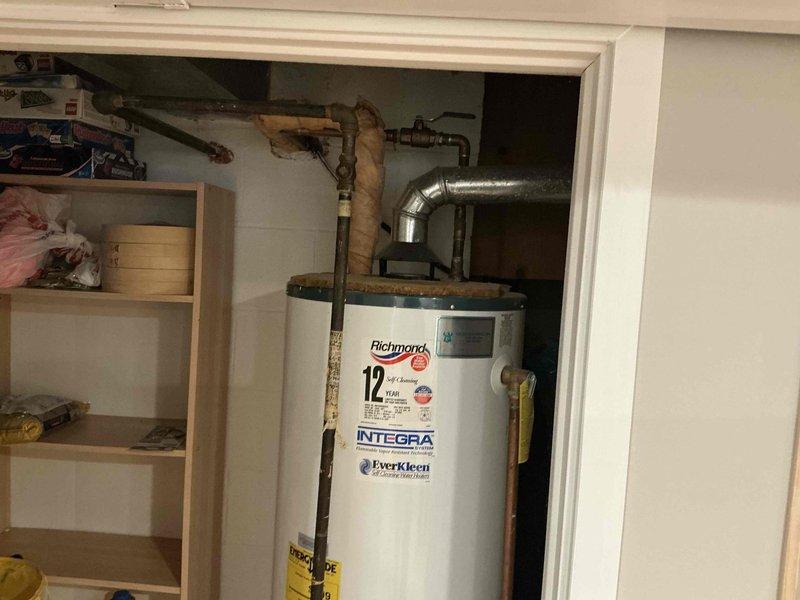 Conducted an indoor air quality assessment in a residential property, focusing on the utility area containing a Richmond water heater with "INTEGRA" technology and "EverKleen" features. Inspected the mechanical room and basement area for ventilation concerns, noting the condition of ductwork, plumbing infrastructure, and storage arrangement that could impact air circulation. Documented existing setup with photographs for reference in developing appropriate IAQ improvement recommendations.