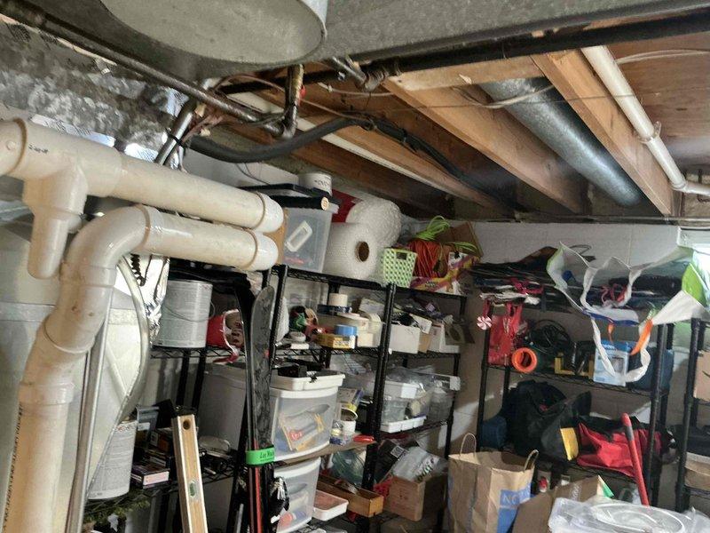 Conducted an indoor air quality assessment in a residential property, focusing on the utility area containing a Richmond water heater with "INTEGRA" technology and "EverKleen" features. Inspected the mechanical room and basement area for ventilation concerns, noting the condition of ductwork, plumbing infrastructure, and storage arrangement that could impact air circulation. Documented existing setup with photographs for reference in developing appropriate IAQ improvement recommendations.