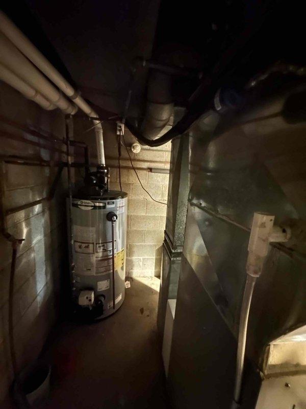 Conducted an assessment of existing HVAC system for potential replacement. Inspected aging water heater and mechanical components in utility room, noting confined installation space with concrete block walls and multiple connected pipes. Evaluated outdoor AC unit showing signs of weather exposure and snow accumulation, currently installed on concrete pad adjacent to residence. System replacement would require careful consideration of existing utility room constraints and proper sizing for the home's requirements.