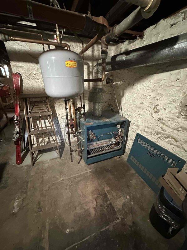 Conducted comprehensive inspection of existing boiler system in basement utility area. Identified aged blue boiler unit with exposed internal components and wiring requiring attention. Noted copper piping configuration, expansion tank mounting, and electrical connections for evaluation of replacement options.