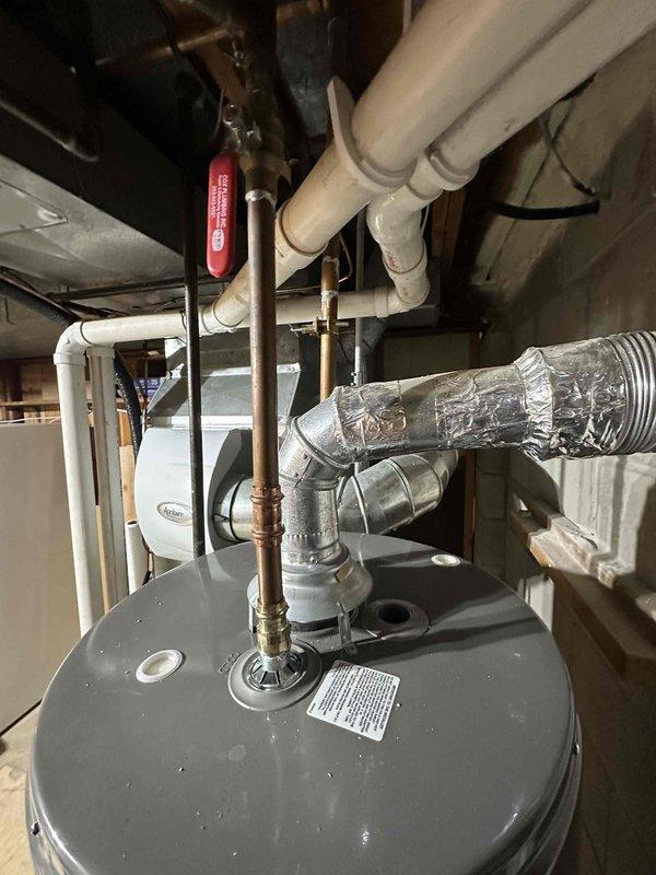 Conducted inspection of residential water heating system in utility area, documenting proper installation of water heater with associated copper and PVC piping infrastructure. Examined electrical circuit breaker panel on concrete block wall, verifying appropriate connections and breaker configuration for the HVAC system.