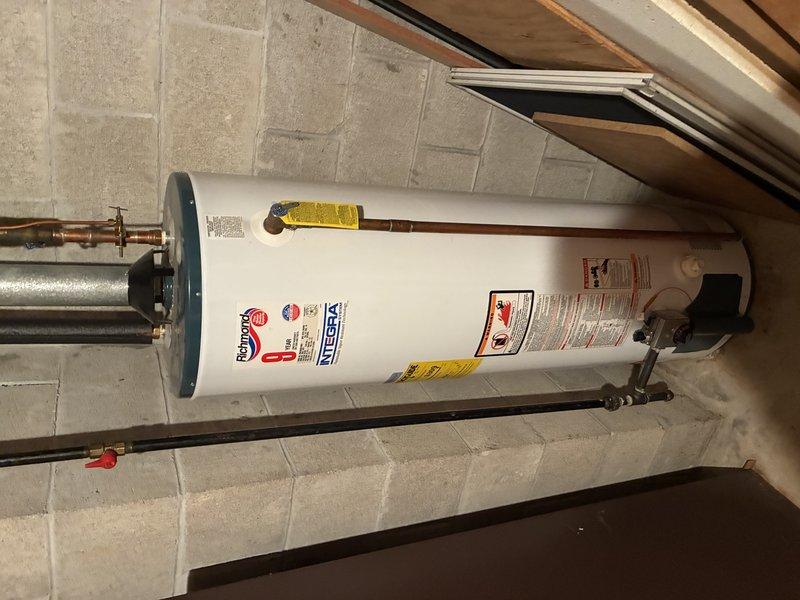 Performed inspection of existing water heater installation. Unit appears to be properly installed with required copper piping connections and pressure relief valve in place. Examined surrounding structural elements including joists and PVC plumbing lines. Water heater is positioned correctly against concrete block wall with all manufacturer labels intact and no visible leaks or damage.