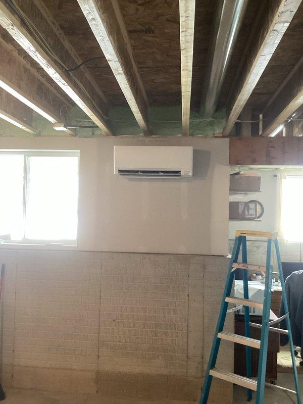 Completed installation of Mitsubishi Electric mini-split system with outdoor condenser unit properly set on concrete pad with gravel base. Indoor head unit was wall-mounted in construction space with exposed ceiling joists. System was pressure tested, evacuated, and charged according to manufacturer specifications with final diagnostic verification confirming proper operation.