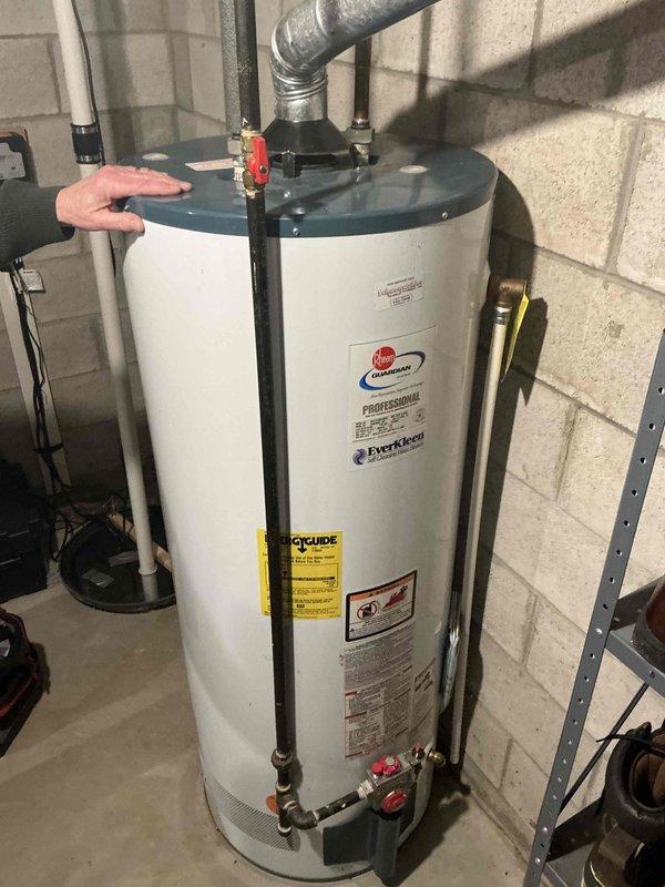 Conducted inspection of existing ductwork system and water heater. Observed aged metal ductwork with significant dust accumulation installed within wooden framing structure. Noted Rheem Professional water heater in functional condition with proper ventilation and supply line connections mounted against concrete block wall in utility area.