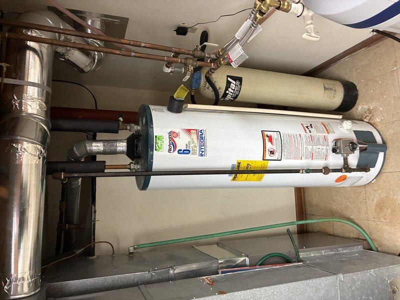 Completed water heater installation in residential utility area with proper copper and PVC plumbing connections. System includes integrated filtration unit mounted above the heater. Inspected adjacent structural areas including joists and existing PVC drainage lines to ensure proper integration with new installation.