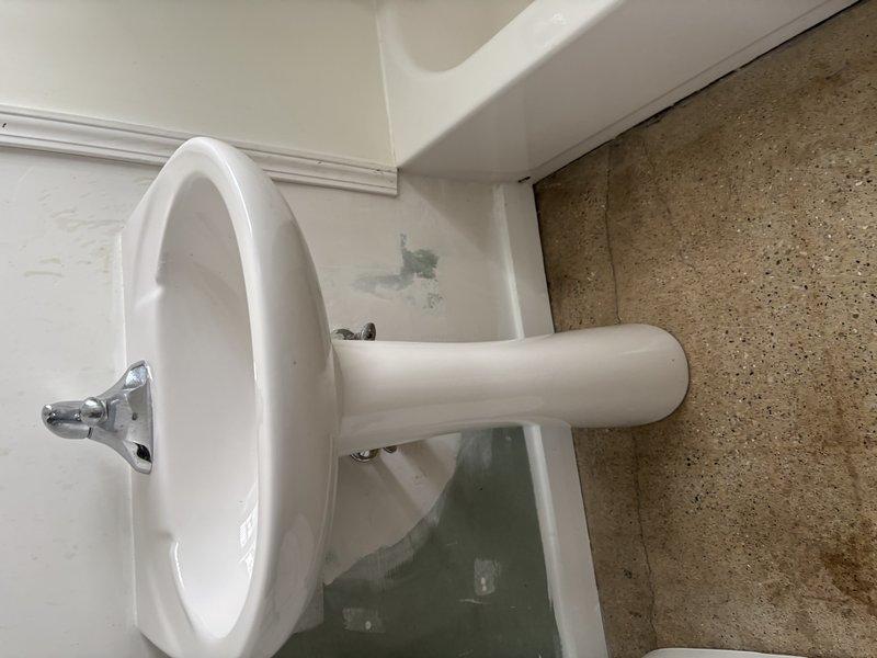 Inspected bathroom fixtures including pedestal sink and surrounding area. Identified minor water damage and discoloration where sink meets wall and floor. No significant plumbing issues with toilet visible in assessment photos, though partial view suggests standard installation and condition.